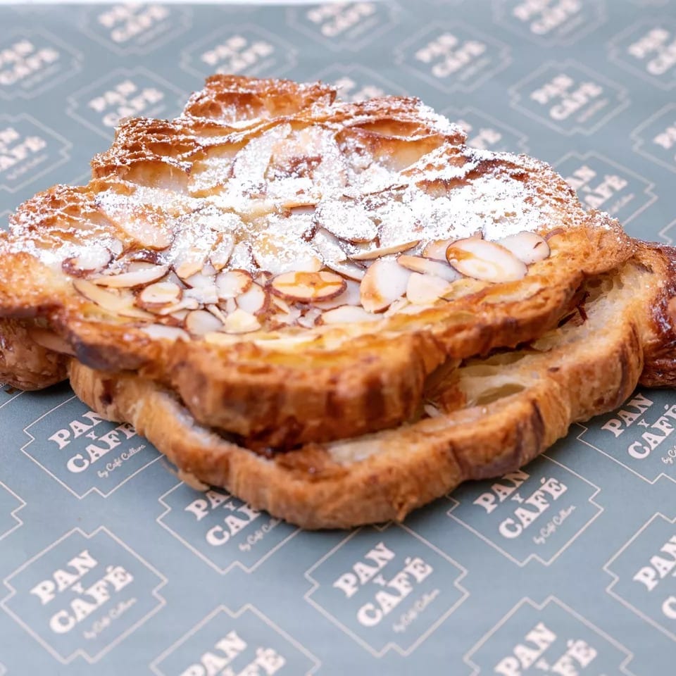 Almond croissant with powdered sugar and sliced almonds on Pan y Café branded paper.
