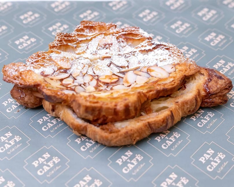 Almond croissant with powdered sugar and sliced almonds on Pan y Café branded paper.