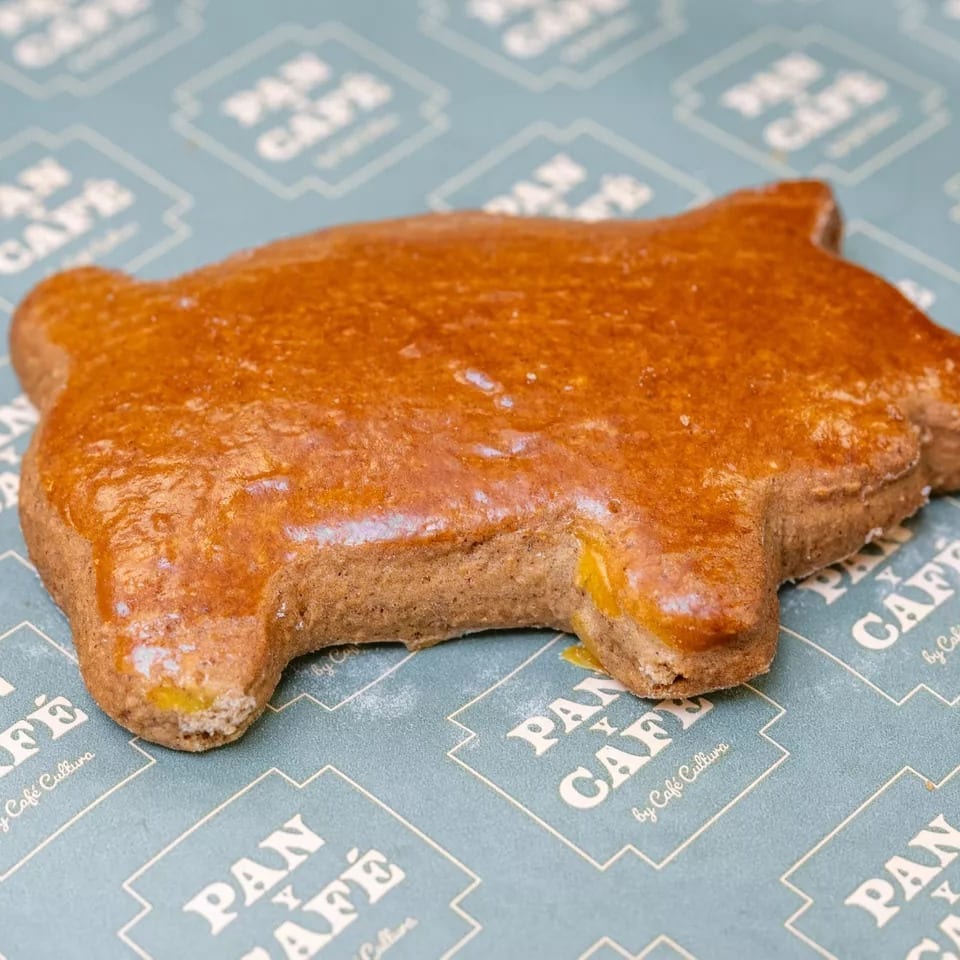 A pig-shaped gingerbread cookie with a shiny glaze rests on Pan y Café branded paper.