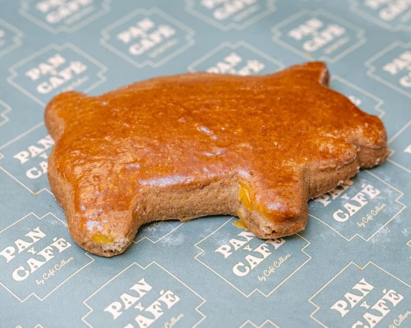 A pig-shaped gingerbread cookie with a shiny glaze rests on Pan y Café branded paper.