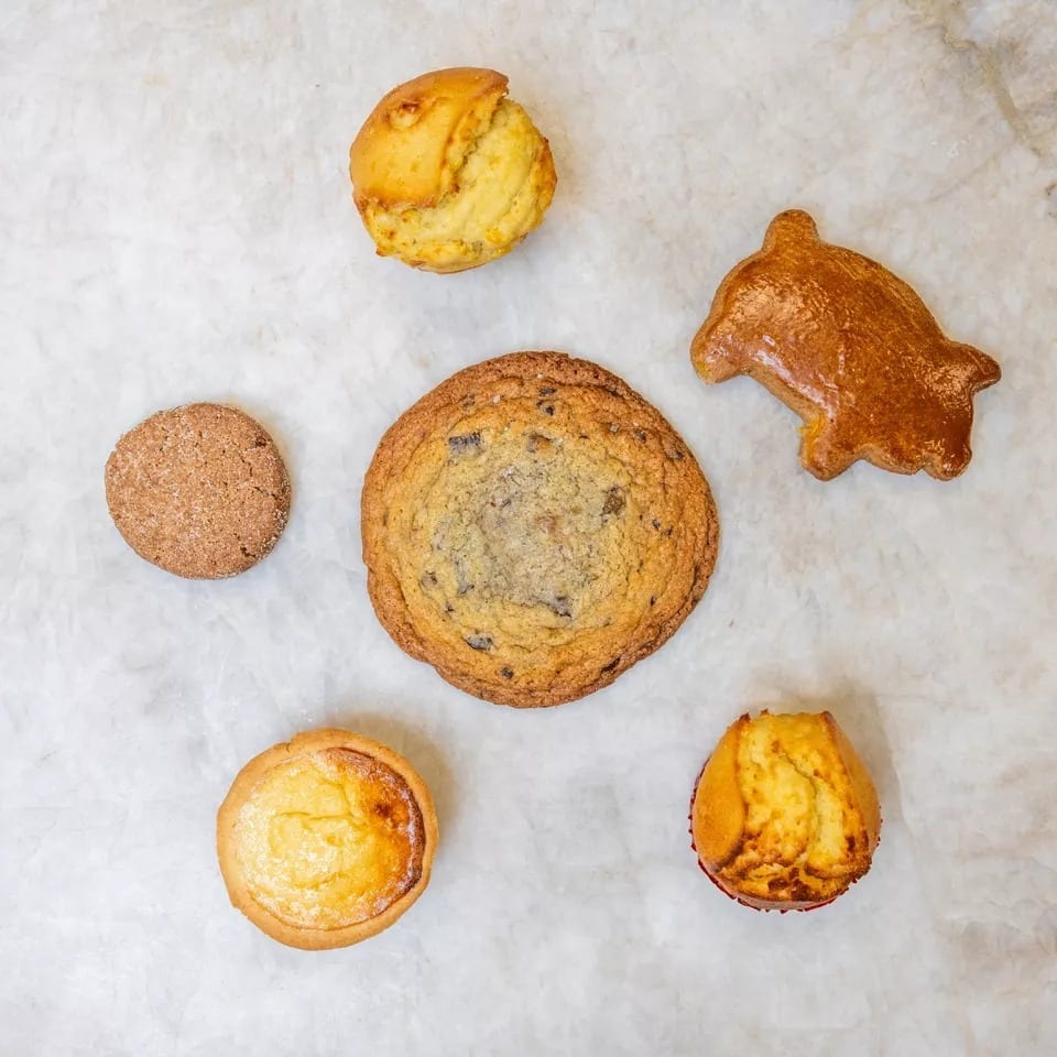 Assortment of baked goods including cookies, muffins, and a pastry on a white marble surface.