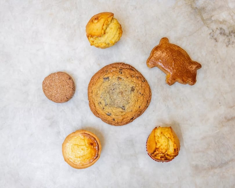 Assortment of baked goods including cookies, muffins, and a pastry on a white marble surface.
