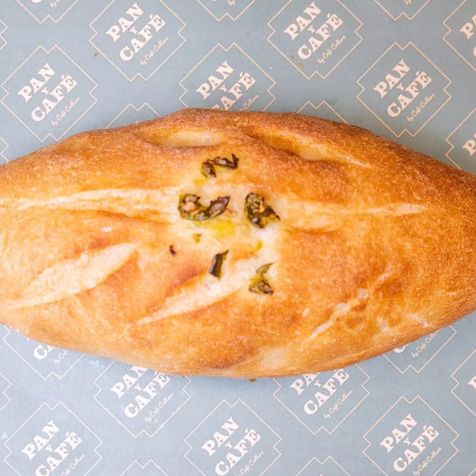 Golden-brown Pan y Café bread with green herbs on light blue branded paper.