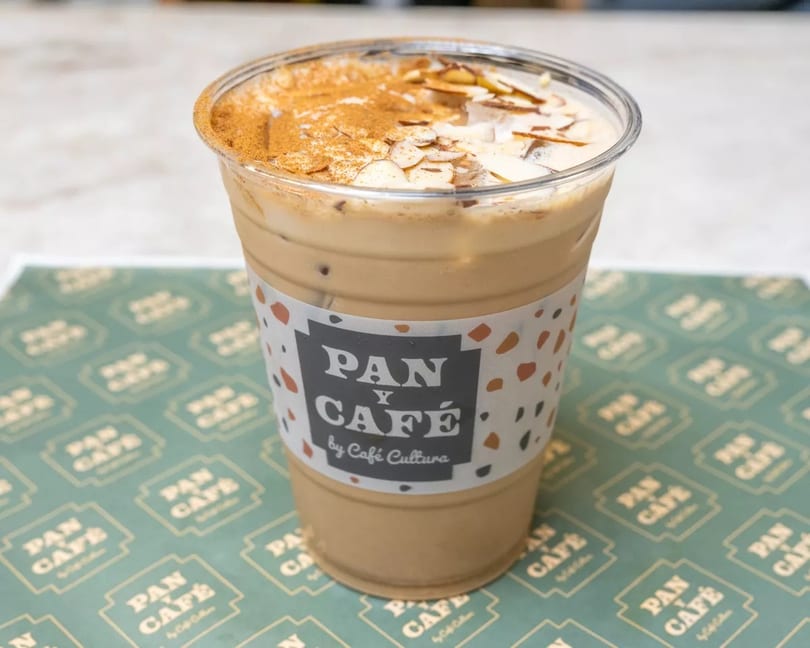 Iced coffee with a Pan y Café by Café Cultura sleeve, topped with cinnamon and almonds.
