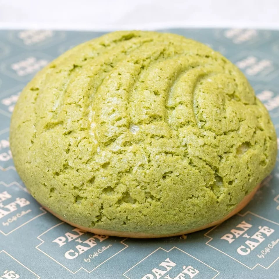 A vibrant green matcha melon pan, a sweet bun with a cookie crust, on branded Pan y Café paper.