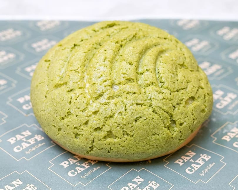 A vibrant green matcha melon pan, a sweet bun with a cookie crust, on branded Pan y Café paper.