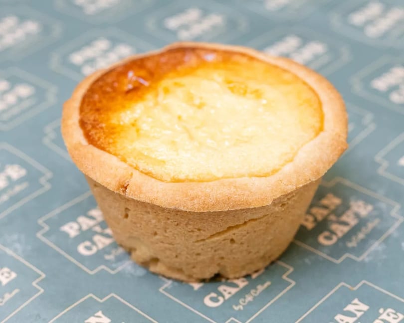 A golden-brown baked cheese tart with a flaky crust sits on a blue patterned surface.