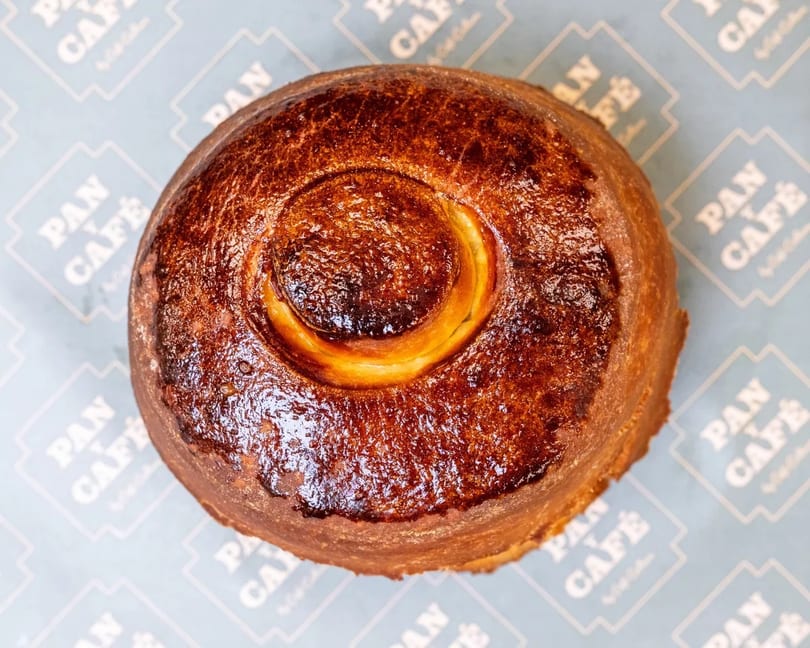 Golden brown, round Pan y Café pastry with a central swirl, on branded paper.